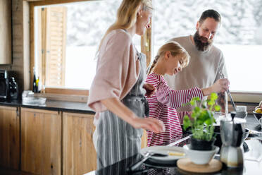 Glückliche Familie mit kleiner Tochter, die im Haus kocht, Winterurlaub in einer Privatwohnung. - HPIF06609