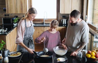 Glückliche Familie mit kleiner Tochter, die im Haus kocht, Winterurlaub in einer Privatwohnung. - HPIF06610