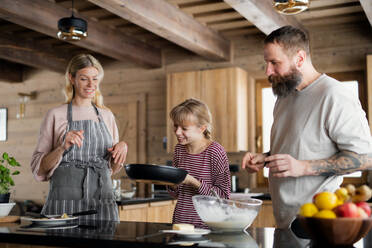 Glückliche Familie mit kleiner Tochter, die im Haus kocht, Winterurlaub in einer Privatwohnung. - HPIF06612