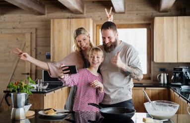 A young family captures a cozy winter moment while cooking together in their private apartment, with their daughter taking a selfie - HPIF06613