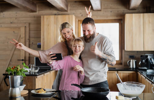 Eine junge Familie fängt einen gemütlichen Wintermoment ein, während sie gemeinsam in ihrer Privatwohnung kocht und ihre Tochter ein Selfie macht - HPIF06613