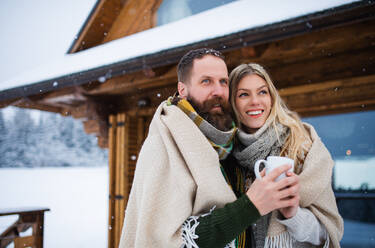 A portrait of happy mature couple in love enjoying holiday in mountain hut, standing outdoors. - HPIF06627