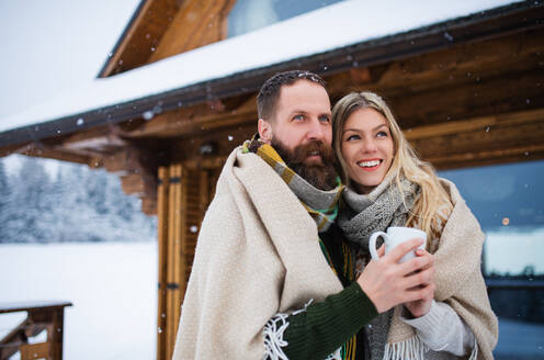 Ein Porträt eines glücklichen, verliebten Paares, das seinen Urlaub in einer Berghütte genießt, im Freien stehend. - HPIF06627