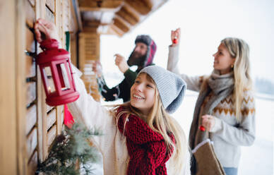 Happy family with small daughter decorating terrace of house outdoors in winter, Christmas time. - HPIF06636