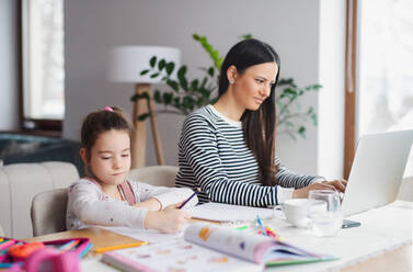 Mother with school girl indoors at home, distance learning and home office concept. - HPIF06650