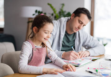 Father helping small daugther with homework indoors at home, distance learning. - HPIF06652