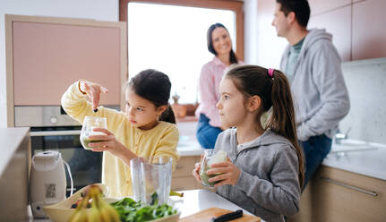 Happy small girls with parents indoors at home, preparing fruit smoothie drink. - HPIF06665