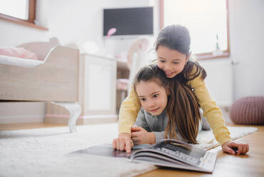 Zwei glückliche kleine Mädchen Schwestern drinnen im Schlafzimmer zu Hause, ein Buch lesen. - HPIF06668