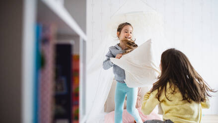 Two cheerful small girls sisters indoors at home, pillow fight on bed in bedroom. - HPIF06669
