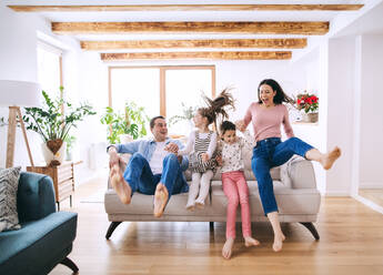 Fröhliche Eltern mit kleinen Töchtern zu Hause, die sich auf dem Sofa amüsieren. - HPIF06672