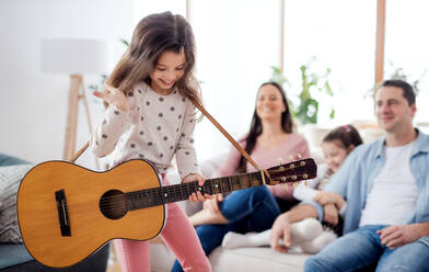 Porträt eines kleinen Mädchens mit Familie zu Hause, das sich mit einer Gitarre vergnügt. - HPIF06675