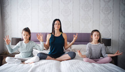 Porträt einer Mutter mit ihren Töchtern bei einer Yoga-Meditationsübung zu Hause. - HPIF06679