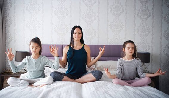 Porträt einer Mutter mit ihren Töchtern bei einer Yoga-Meditationsübung zu Hause. - HPIF06679