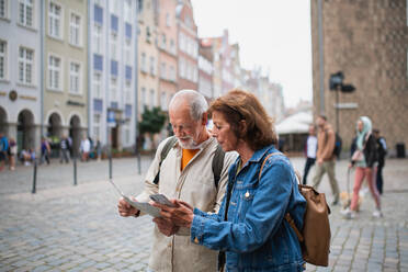 Ein Porträt eines älteren Touristenpaares, das eine Karte und ein Smartphone im Freien auf einer Straße in der Stadt benutzt - HPIF06695