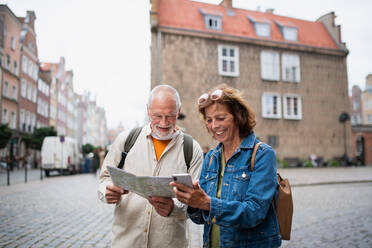 A portrait of happy senior couple tourists using map outdoors in town street - HPIF06696