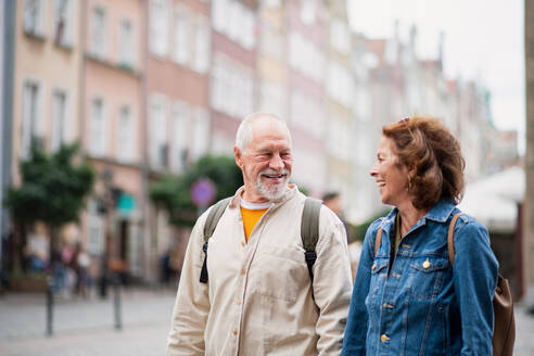 Ein Porträt eines glücklichen älteren Paares, das sein Smartphone im Freien in einer historischen Stadt benutzt - HPIF06698