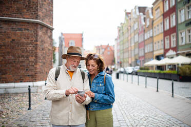 A portrait of happy senior couple tourists using smartphone outdoors in historic town - HPIF06700