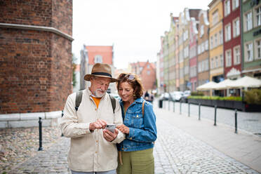 Ein Porträt eines glücklichen älteren Paares, das sein Smartphone im Freien in einer historischen Stadt benutzt - HPIF06700