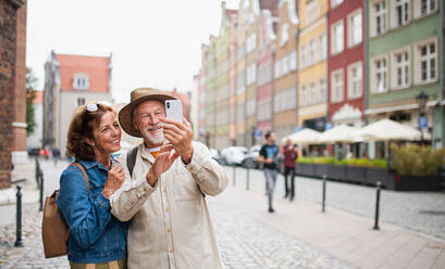 A joyful elderly couple captures a memory with a selfie in a charming historic town during their travels - HPIF06702