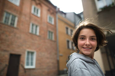 Ein Porträt eines glücklichen Mädchens im Teenageralter, das sich umdreht und in die Kamera schaut, draußen auf der Straße. - HPIF06717