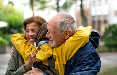 Glückliche Großeltern mit einer Enkeltochter im Teenageralter, die sich auf der Straße in der Stadt umarmen - HPIF06734
