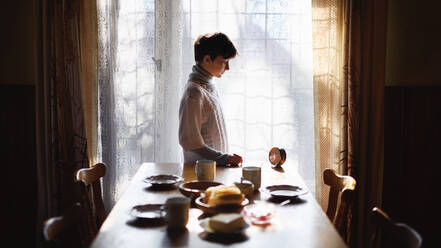 Portrait of poor sad small girl setting table indoors at home, poverty concept. - HPIF06741