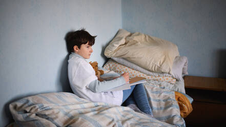 Poor sad small girl sitting on bed indoors at home, poverty concept. - HPIF06763