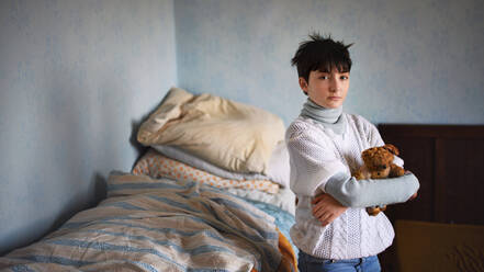 Poor sad small girl with teddy bear standing and looking at camera indoors at home, poverty concept. - HPIF06764