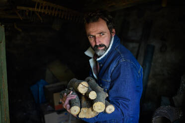 Armer reifer Mann beim Sammeln von Brennholz in einem Schuppen zu Hause, Konzept der Armut. - HPIF06793