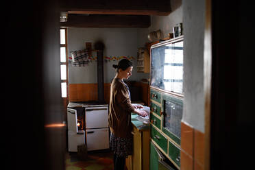 A portrait of poor mature woman indoors at home washing dishes, poverty concept. - HPIF06799