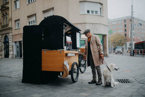 Eleganter älterer Mann geht mit seinem Hund spazieren und kauft Straßenkaffee im Freien in der Stadt. - HPIF06842
