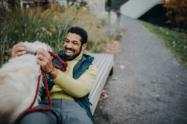 Happy young man training and cuddling with his dog outdoors in city park, during a cold autumn day. - HPIF06849