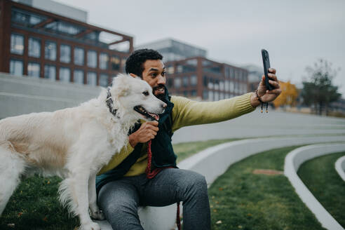 A cheerful man captures a moment with his furry friend in a city park on a chilly autumn day - HPIF06850