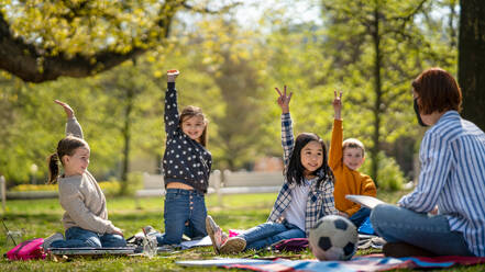 A teacher with small children sitting outdoors in city park, learning group education and art concept. - HPIF06860