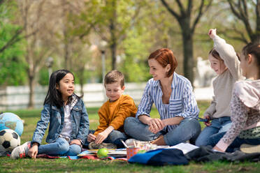 Ein Lehrer mit kleinen Kindern, die im Freien im Stadtpark sitzen und das Konzept der Gruppenbildung lernen. - HPIF06866