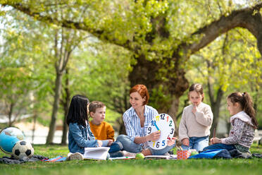 Ein Lehrer mit kleinen Kindern, die im Freien im Stadtpark sitzen und das Konzept der Gruppenbildung lernen. - HPIF06868