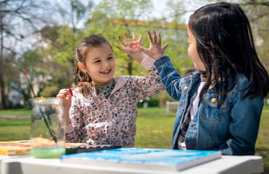 Portrait of small children painting pictures outdoors in city park, learning group education concept. - HPIF06871