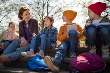 Ein Lehrer mit kleinen Kindern, die im Freien im Stadtpark sitzen und das Konzept der Gruppenbildung lernen. - HPIF06884