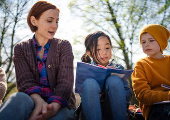 Ein Lehrer mit kleinen Kindern, die im Freien im Stadtpark sitzen und das Konzept der Gruppenbildung lernen. - HPIF06885