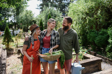 A happy farmer family holding their harvest in basket outdoors in garden. - HPIF06896