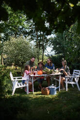 Eine glückliche Bauernfamilie sitzt am Tisch und betrachtet ihre Ernte im Freien auf dem Gemeinschaftshof. - HPIF06903