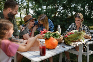 A happy farmer family sitting at table and looking at their harvest outdoors in garden. - HPIF06904