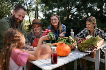 A happy family of farmers sitting by the table and looking at their harvest outdoors at community farm. - HPIF06905