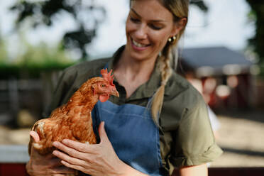 Eine fröhliche Bäuerin hält ein Huhn im Freien auf einem Bauernhof. - HPIF06923