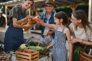 Ein kleines Mädchen mit seiner Mutter streichelt ein Huhn auf dem Bauernmarkt. - HPIF06924