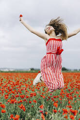 Fröhliche junge Frau springt auf Mohnfeld - JJF00331