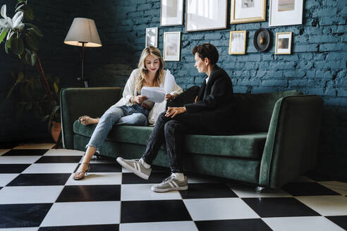 Actress reading script sitting with producer on sofa at film set - MDOF00683