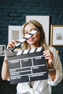 Smiling actress holding clapboard on film set - MDOF00698