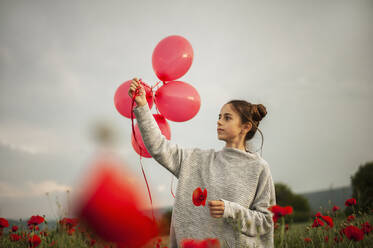 Nachdenkliches Mädchen mit Mohnblume hält rote Luftballons unter dem Himmel - ALKF00140