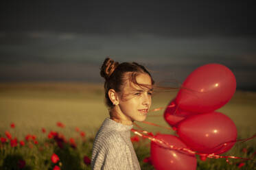 Nachdenklich lächelndes Mädchen mit Luftballons auf einem Mohnfeld - ALKF00142